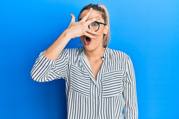 Young caucasian woman wearing business shirt and glasses peeking in shock covering face and eyes with hand, looking through fingers afraid