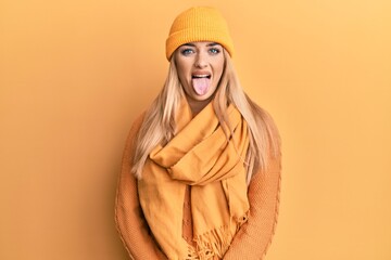 Young caucasian woman wearing wool winter sweater and cap sticking tongue out happy with funny expression. emotion concept.