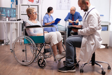 Medical physician discussing with handicapped senior woman sitting in wheelchair. Man with disabilities ,walking frame sitting in hospital bed. Health care system, clinic patients.