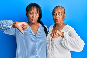 Hispanic family of mother and daughter hugging together with love with angry face, negative sign...