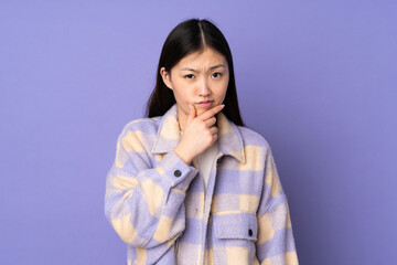 Young asian woman isolated on purple background having doubts