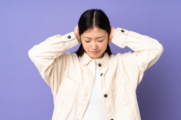 Young asian woman isolated on purple background frustrated and covering ears