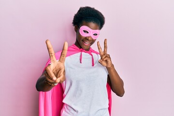 Young african american girl wearing superhero mask and cape costume smiling looking to the camera showing fingers doing victory sign. number two.