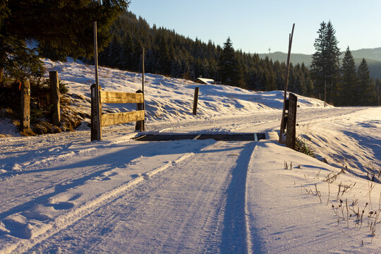 Tranquil snow covered landscape at sunset in wintertime with snowy road and cattle guard in the alps (Filzmoos, Salzburg county, Austria)