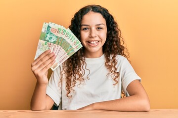 Teenager hispanic girl holding 50 hong kong dollars banknotes looking positive and happy standing and smiling with a confident smile showing teeth