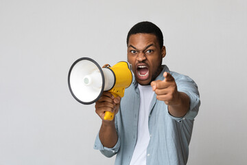 Young black man shouting in megaphone over grey background