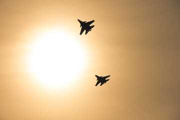 Two plane silhouettes in the sky against the bright sun