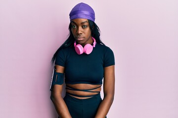 Young african american woman wearing gym clothes and using headphones skeptic and nervous, frowning upset because of problem. negative person.
