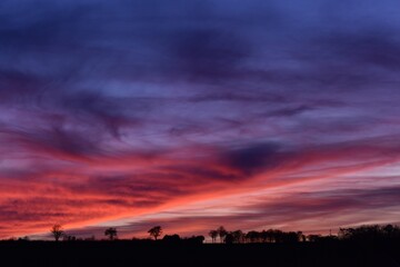 Fiery autumn sunset above the black silhouette of typical French countryside in Burgundy, France, putting up a spectacular display of pink, purple and red