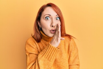 Beautiful redhead woman wearing casual winter sweater over yellow background hand on mouth telling secret rumor, whispering malicious talk conversation