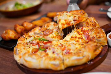 scooping hawaiian half deluxe pizza dough thick and soft to stretch cheese on tray with grilled chicken drumstick barbecue for lunch or breakfast and dinner to family eating food at italian restaurant