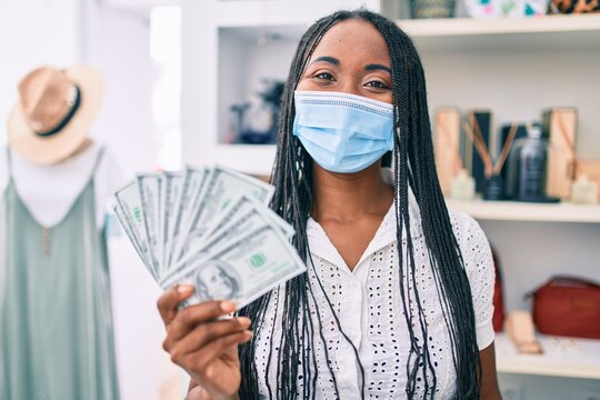 Young african american woman wearing medical mask holding dollars banknotes at clothing store