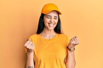 Young hispanic woman wearing delivery uniform and cap excited for success with arms raised and eyes closed celebrating victory smiling. winner concept.