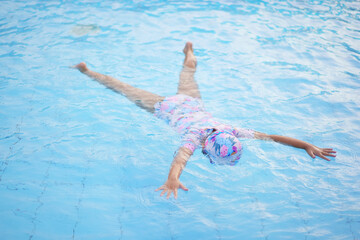 Asian child cute or kid girl floating in water by spread arms and legs to pretends starfish upside down on swimming pool for learn and funny training swim or refreshing and exercise on summer school