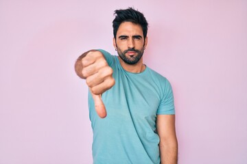 Fototapeta premium Handsome hispanic man with beard wearing casual clothes looking unhappy and angry showing rejection and negative with thumbs down gesture. bad expression.