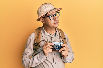 Middle age bald man wearing explorer hat and vintage camera smiling looking to the side and staring away thinking.