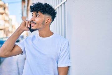 Young arab man smiling happy talking on the smartphone leaning on the wall.