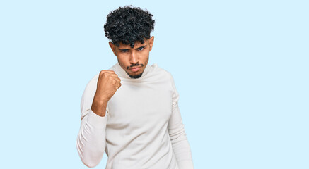 Young arab man wearing casual winter sweater angry and mad raising fist frustrated and furious while shouting with anger. rage and aggressive concept.