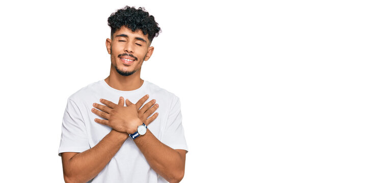 Young arab man wearing casual white t shirt smiling with hands on chest with closed eyes and grateful gesture on face. health concept.