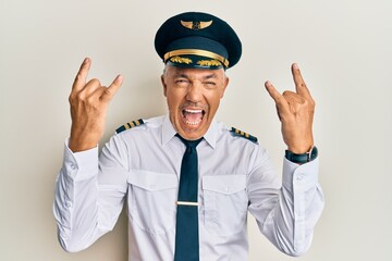 Handsome middle age mature man wearing airplane pilot uniform shouting with crazy expression doing rock symbol with hands up. music star. heavy music concept.