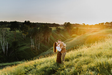 Beautiful young woman and a man walk, hug and kiss in nature at sunset.