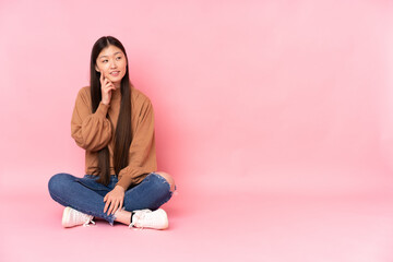Obraz na płótnie Canvas Young asian woman sitting on the floor isolated on pink background thinking an idea while looking up