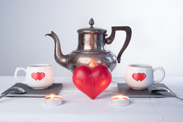 Teapot and two cups with hearts painted on them., a red love heart in the middle and two lighted candles. Romantic tea time or breakfast. Concept of love and Valentines day 