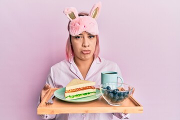 Hispanic woman with pink hair wearing pajama holding healthy breakfast depressed and worry for distress, crying angry and afraid. sad expression.