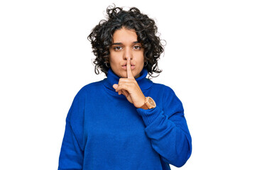 Young hispanic woman with curly hair wearing turtleneck sweater asking to be quiet with finger on lips. silence and secret concept.