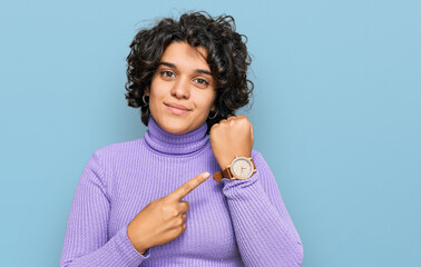 Young hispanic woman with curly hair wearing casual clothes in hurry pointing to watch time,...