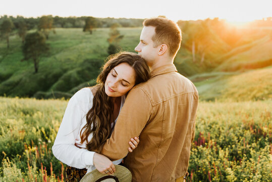 Beautiful young woman and a man walk, hug and kiss in nature at sunset.