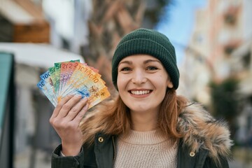 Young caucasian girl smiling happy holding swiss franc banknotes at the city.