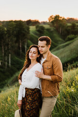 Beautiful young woman and a man walk, hug and kiss in nature at sunset.