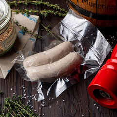 White pudding sausages in a vacuum package on wooden table with seasonings and herbs around, top...