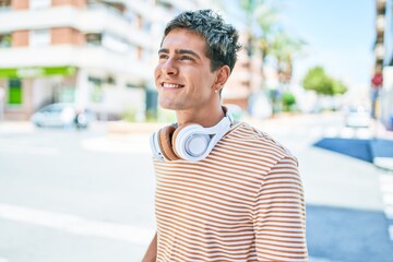 Young handsome caucasian man smiling happy wearing headphones walking at city.