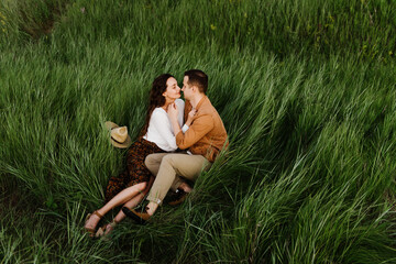 Beautiful young woman and man hug and kiss in the tall grass in summer.