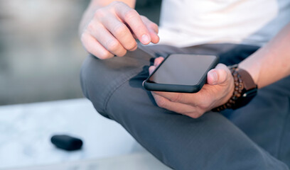 Closeup shot of man hands holding blank screen smartphone while sitting outdoors.