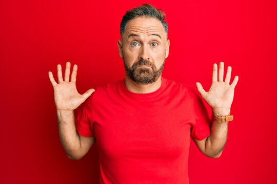Handsome middle age man wearing casual red tshirt clueless and confused with open arms, no idea and doubtful face.