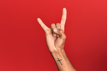 Hand of hispanic man over red isolated background gesturing rock and roll symbol, showing obscene horns gesture