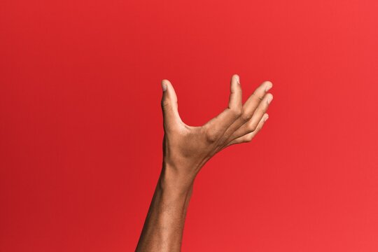 Hand of hispanic man over red isolated background picking and taking invisible thing, holding object with fingers showing space