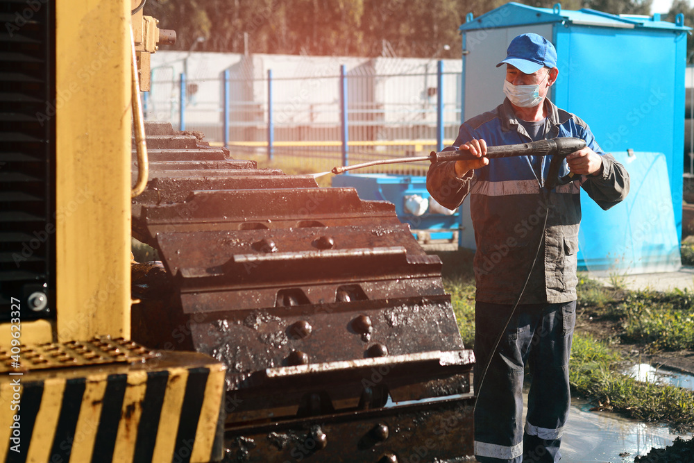 Wall mural The worker washes the tracks of the bulldozer with a water gun under pressure. This is a service for washing heavy machinery and tractors.