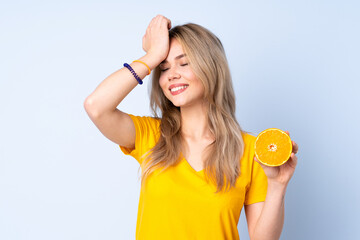 Teenager Russian girl holding an orange isolated on blue background has realized something and intending the solution