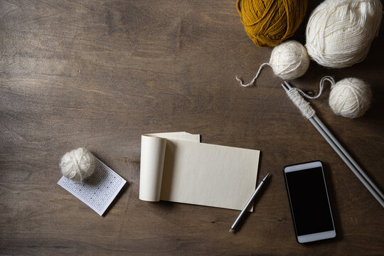 Online courses for learning to crochet. White balls of yarn, knitting needles with a set of thread. Schematic representation of the drawing. Blank pages of a notebook, and mobile devices. Mockup.