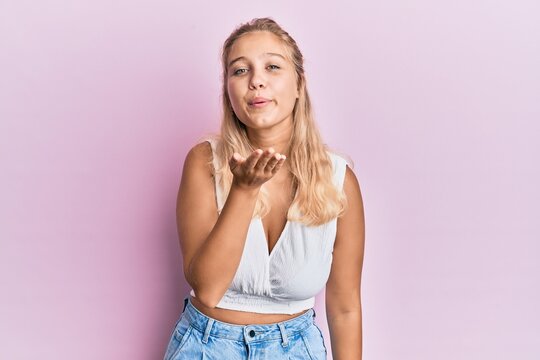 Young blonde girl wearing casual clothes looking at the camera blowing a kiss with hand on air being lovely and sexy. love expression.