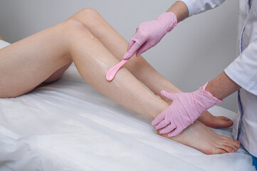 Laser epilation and cosmetology in beauty salon, spa concept. Preparation for the procedure of laser hair removal. Application of gel, disposable spatula. Beautiful smooth female legs.