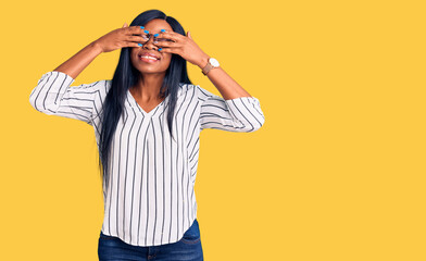 Naklejka premium Young african american woman wearing casual clothes and glasses covering eyes with hands smiling cheerful and funny. blind concept.