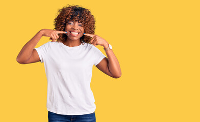 Young african american woman wearing casual white tshirt smiling cheerful showing and pointing with fingers teeth and mouth. dental health concept.