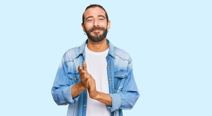 Attractive man with long hair and beard wearing casual denim jacket clapping and applauding happy and joyful, smiling proud hands together