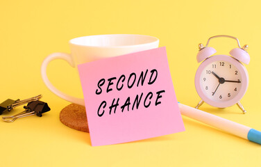 Pink paper with the text SECOND CHANCE on a white cup. Clock, pen on a yellow background.