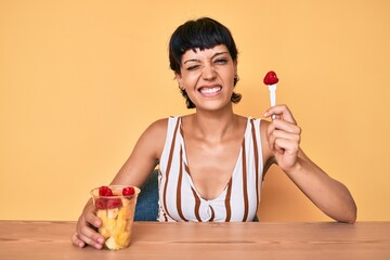 Beautiful brunettte woman eating fresh and healthy fruit winking looking at the camera with sexy...